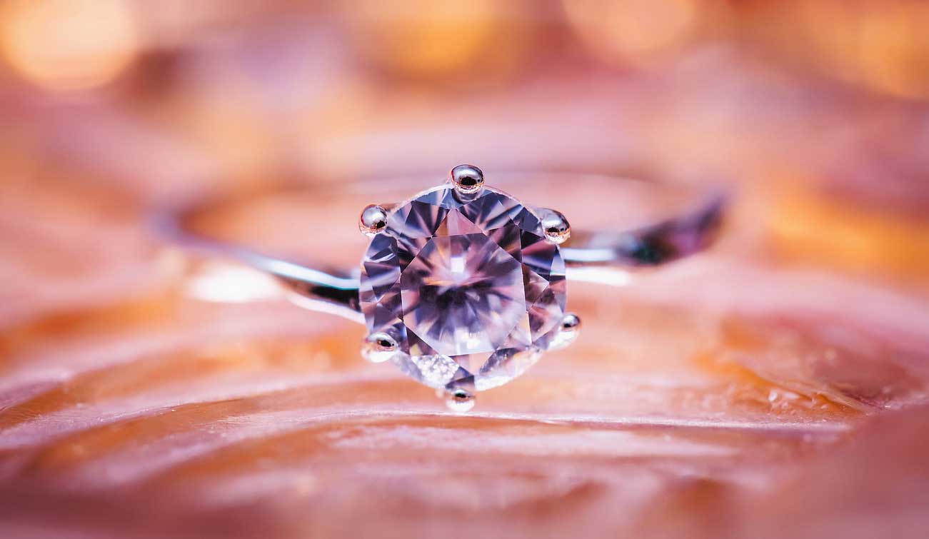 Een handgemaakte zilveren ring met een sprankelende diamant in zes griffen, omlijst door zachte roze en gouden gloed.