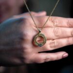 Een open hand toont liefdevol een gouden kettinkje met een uniek ringvormig hangertje en fonkelende edelsteen, warm in het zachte licht.