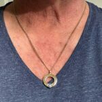 Een warme gloed om haar hals: een gouden ketting met ronde hanger en wit steentje, rustend op haar blauwe V-hals.