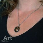 Een close-up van een persoon met goudkleurig lichtbruin haar, een unieke zilveren ketting met ovale steen en warme uitstraling. "Art By Daan" linksonder.