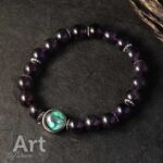 Handgemaakte armband met donkerpaarse kralen en zilveren spacers, uniek glazen middenstuk beschilderd met groene en blauwe acrylverf.